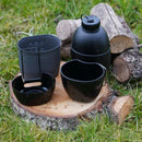 BCB Multi-Fuel Cooking System with aluminum stove, canteen, cup, mug, and multicam pouch on wooden log outdoors.