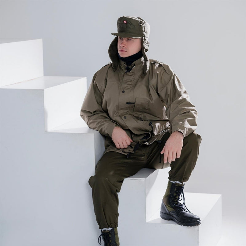 Man wearing genuine Dutch army parka with liner in olive drab green, matching pants, and military-style cap sitting on white steps