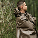 Man leaning against tree wearing a waterproof olive German army rain poncho with hood in a forest setting