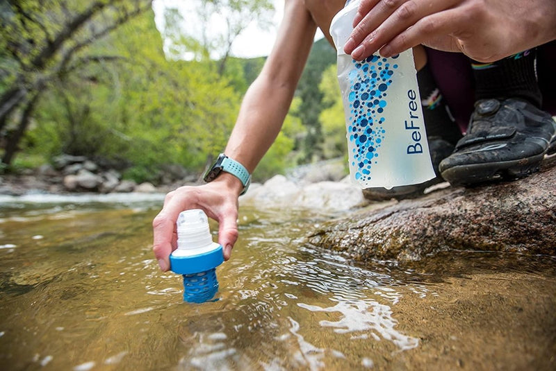 Person filling Katadyn BeFree 0.6L water bottle filter from a clear stream in outdoor setting