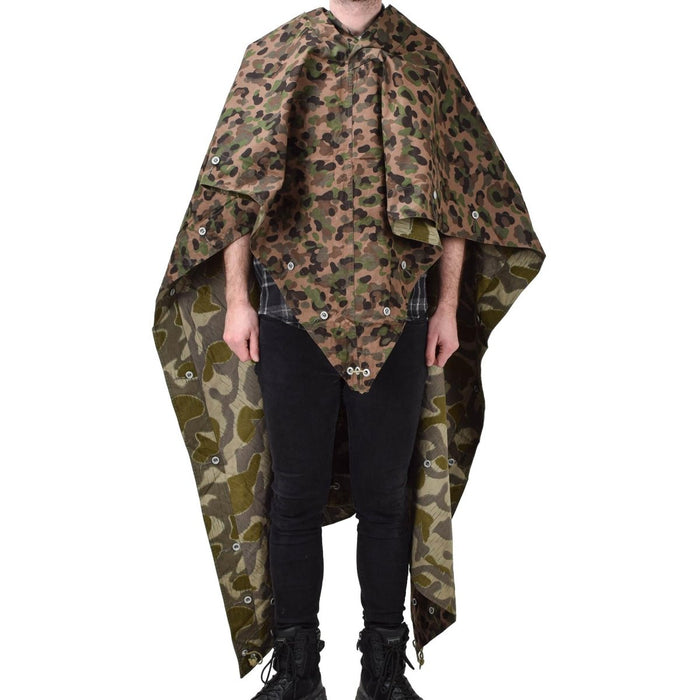Person, die ein wasserabweisendes Vintage-Ponchozelt der österreichischen Armee mit Erbsenmuster und Splittertarn und Eckbändern trägt