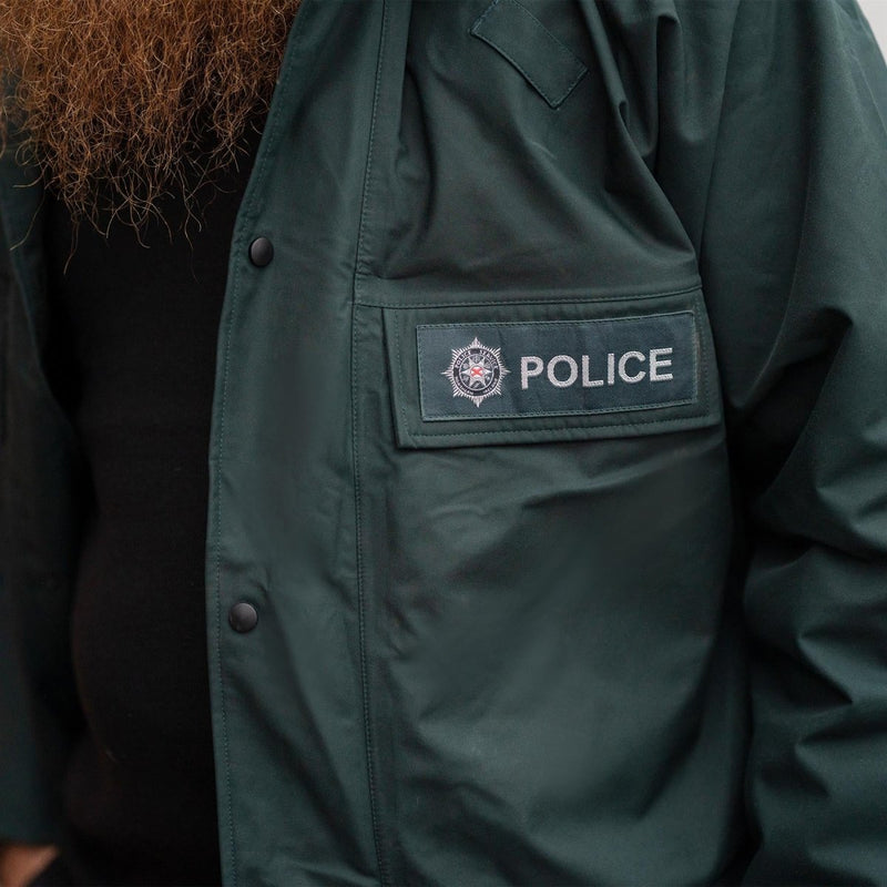 Close-up of original British police green waterproof anorak parka with police badge patch on chest pocket.