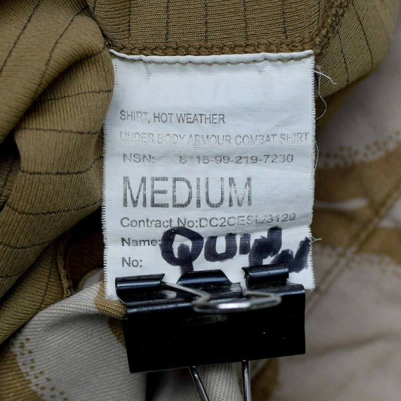 Close-up of a medium original British UBAC desert camouflage under body armor combat shirt label with binder clip attached