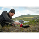 Man outdoors using Primus Essential Trail Stove compact camping gas burner to heat kettle in nature setting