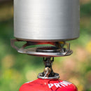 Close-up of a compact Primus Essential Trail Stove burning butane gas with a pot placed on top outdoors.