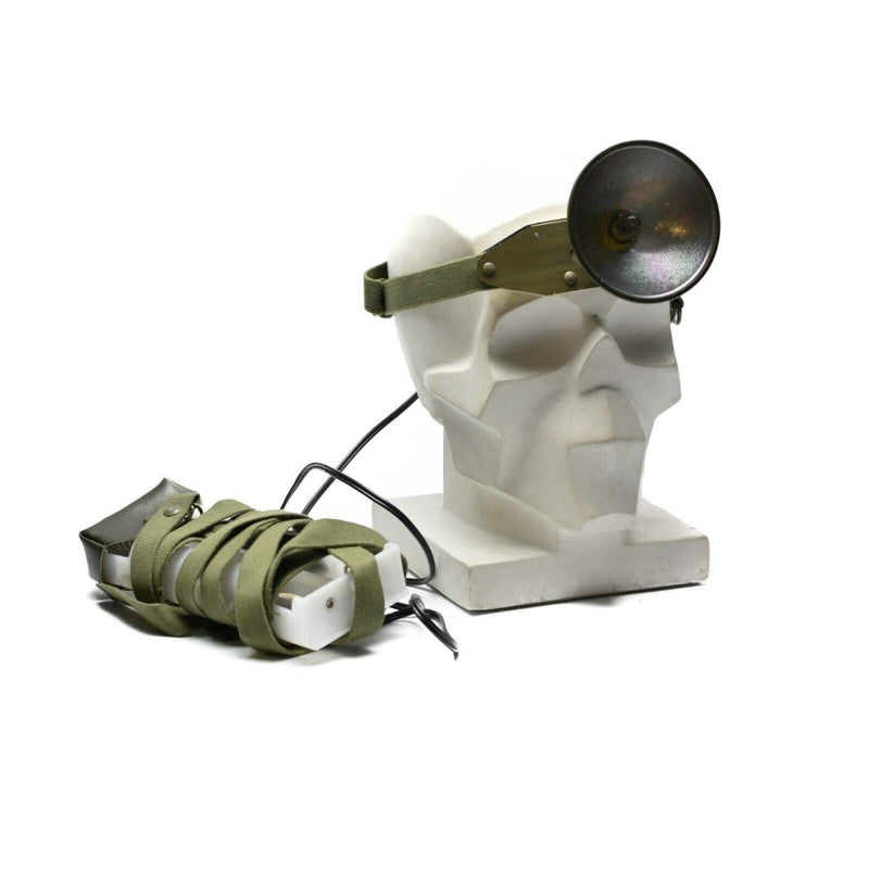 White sculpture with green straps and a black circular headlamp  on a white background